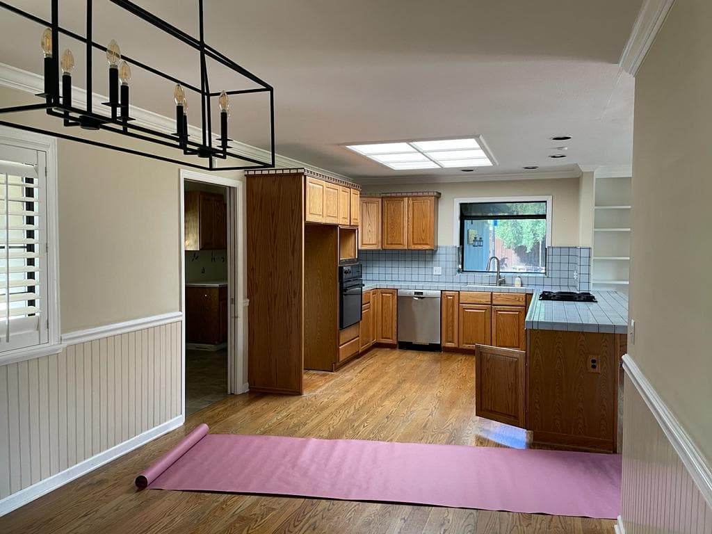 Before: Original closed-layout kitchen before remodel with oak cabinets, blue tile countertops, fluorescent ceiling box, and wall separating dining area