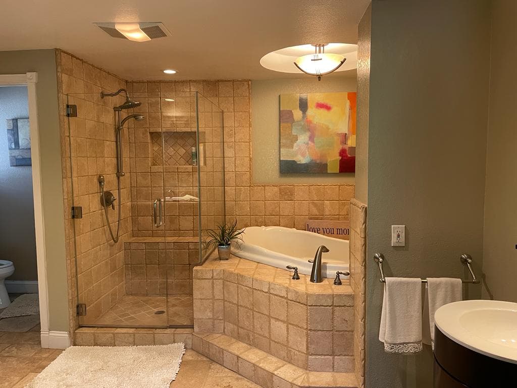 Primary bathroom before remodel with dated travertine tile, drop in tub, and walk in shower
