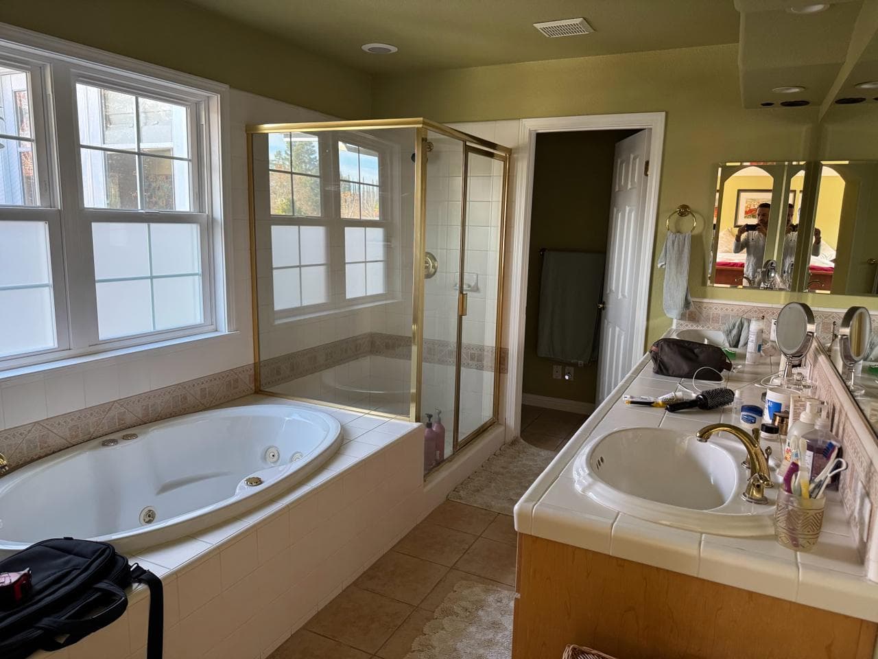 Dated primary bathroom before remodel with built-in jetted tub, gold-framed shower enclosure, olive green walls, and tile countertop vanity