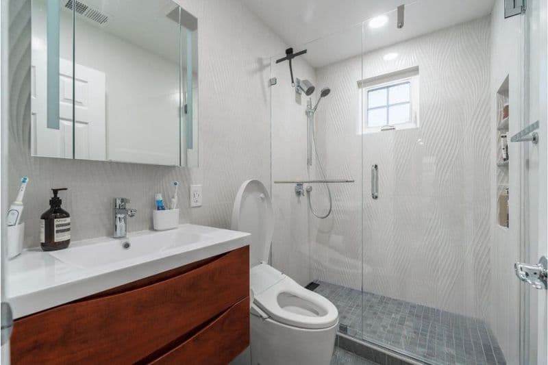 Luxury bathroom remodel in Santa Clara featuring large-format gray porcelain tile, wood-tone floating vanity with undermount sinks, frameless glass shower enclosure, and modern pendant lighting fixtures
