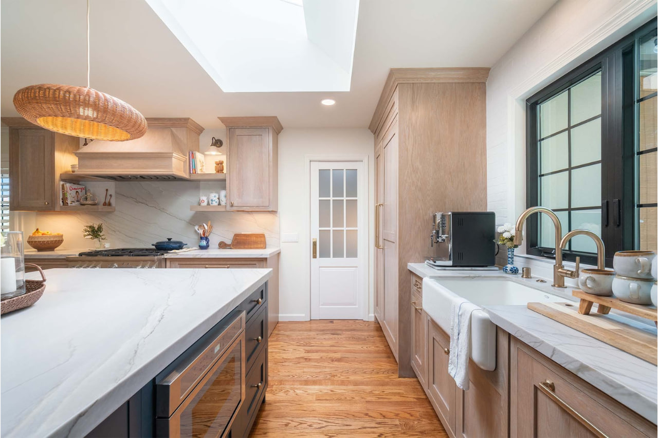 Warm transitional kitchen featuring natural wood lower cabinets, white upper cabinets, skylight, and hardwood floors throughout
