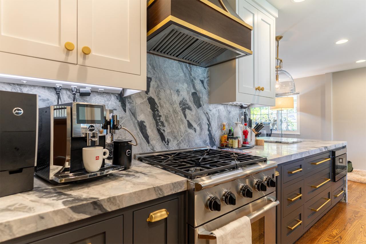 Contemporary kitchen with dramatic marble waterfall island, white and gray cabinetry, and gold accent hardware details