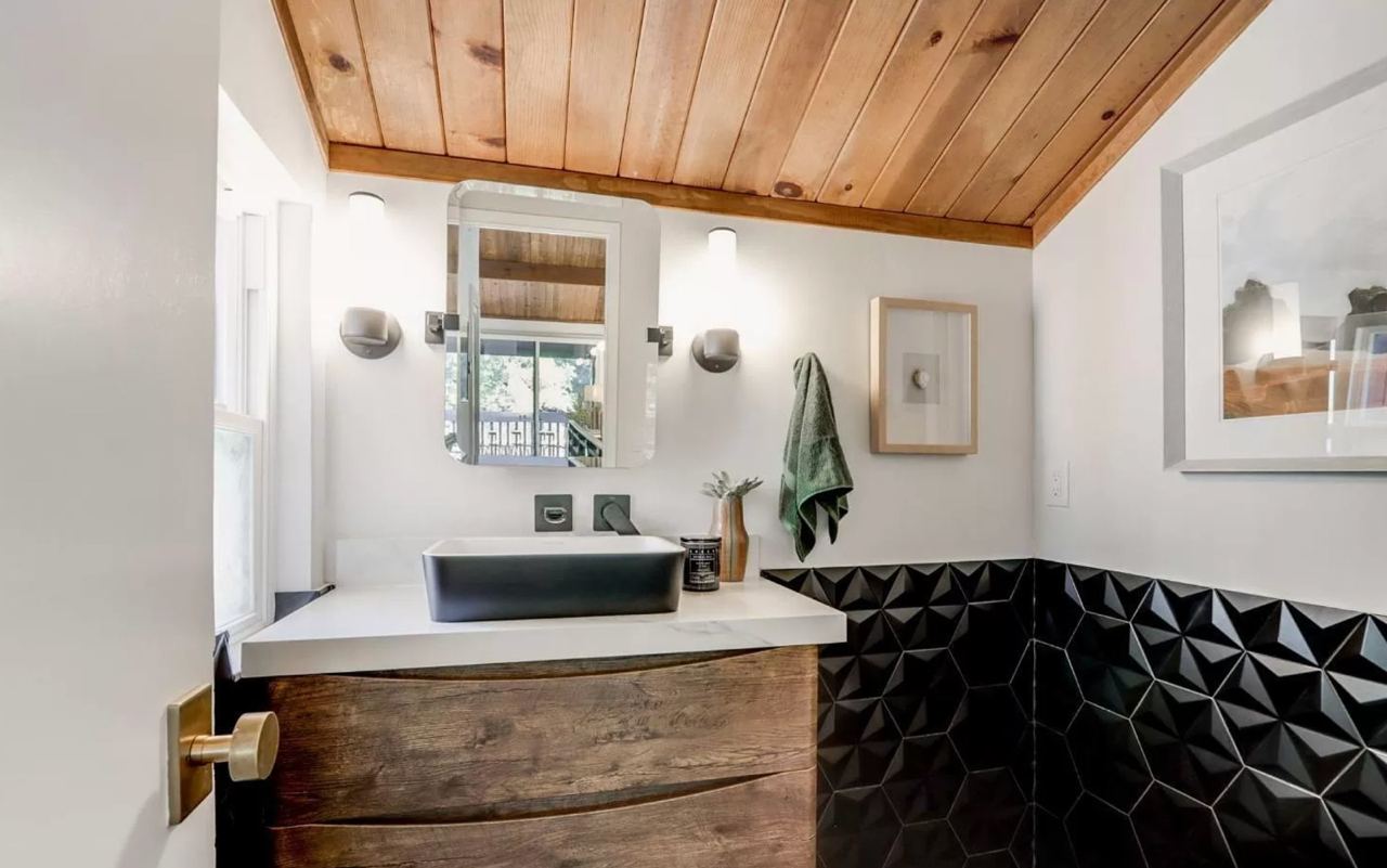Thoughtfully designed bathroom with strategic lighting layouts highlighting vaulted wood ceiling and custom rustic vanity with black grid shower