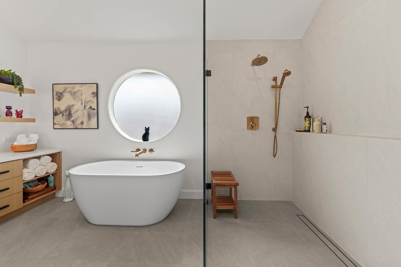 primary bathroom after: freestanding soaking tub with round window with white soaking tub and brushed brass fixtures, by ASL Remodeling, Pacifica.