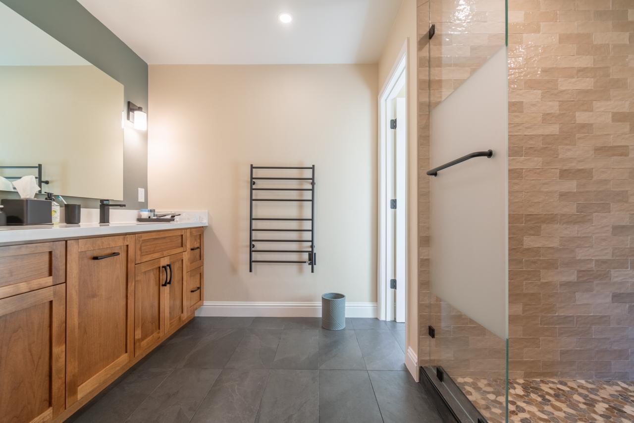 primary bathroom: glass shower with warm stone tile with wood cabinetry and porcelain floor tile, by ASL Remodeling.