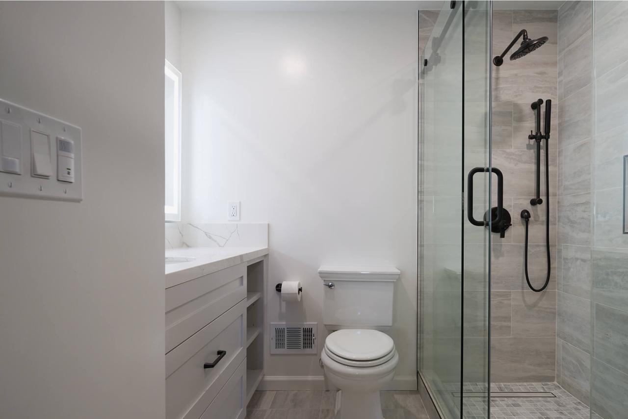 Accessible walk in shower remodel featuring minimalist white porcelain slabs, polished grab bars, slip-resistant flooring, and efficient compact space design.