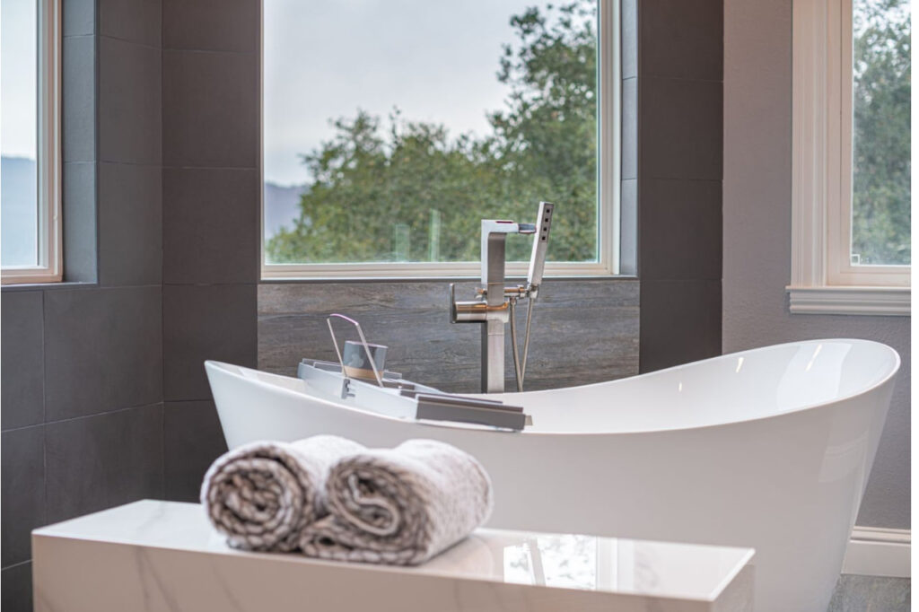 Modern bathroom remodeling in Los Gatos featuring freestanding tub with dark tile accent wall and large picture window