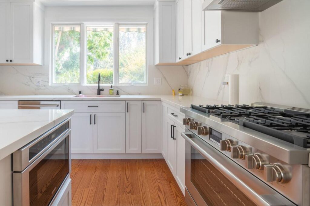 Luxury kitchen remodel featuring expansive quartz countertops on a large kitchen island with recessed lighting and classic white shaker cabinets throughout.