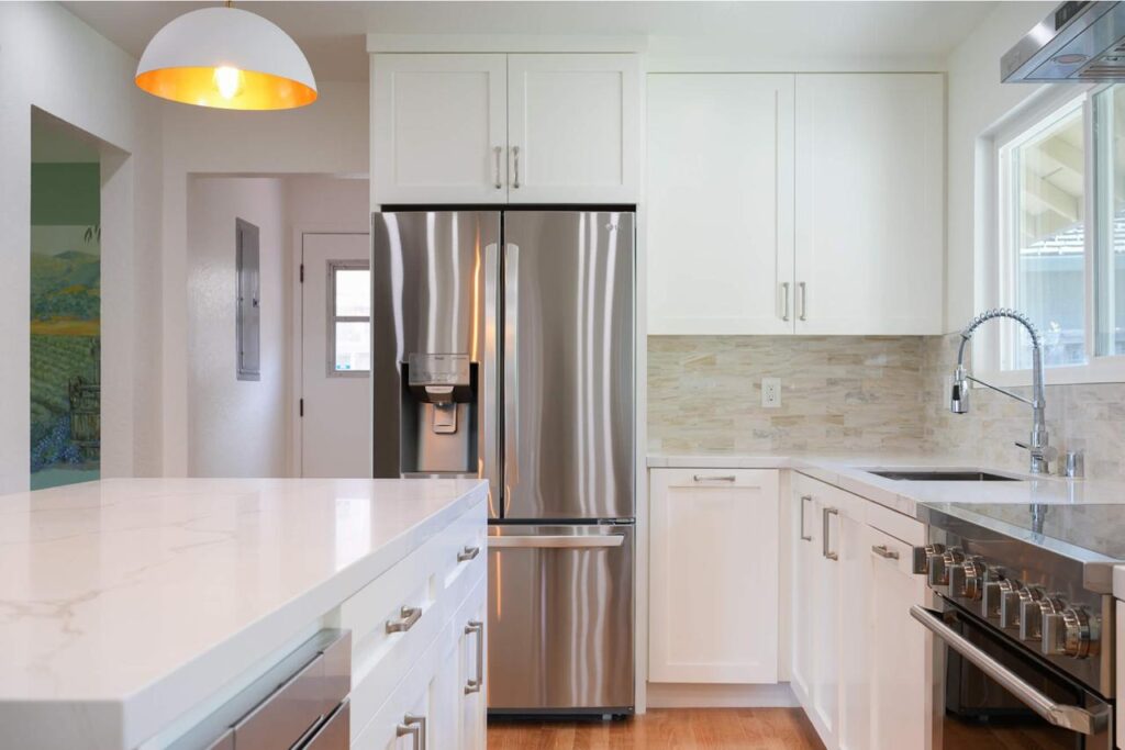 Custom kitchen cabinets in white with dark granite countertops, stainless steel appliances, and statement gold pendant lighting.