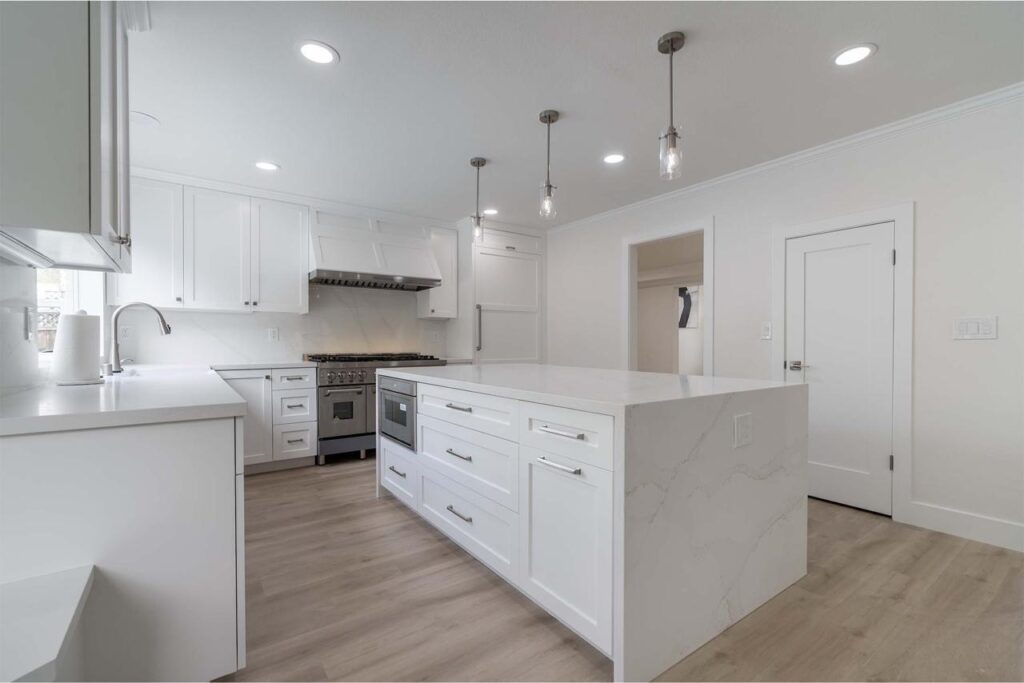 Kitchen and bath remodeling project with white shaker cabinets, island with bar seating, pendant lighting, and bright open layout.