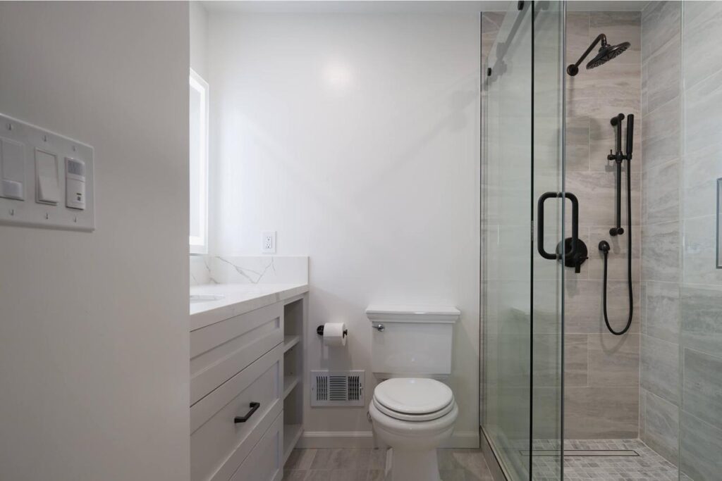 Accessible walk in shower remodel featuring minimalist white porcelain slabs, polished grab bars, slip-resistant flooring, and efficient compact space design.