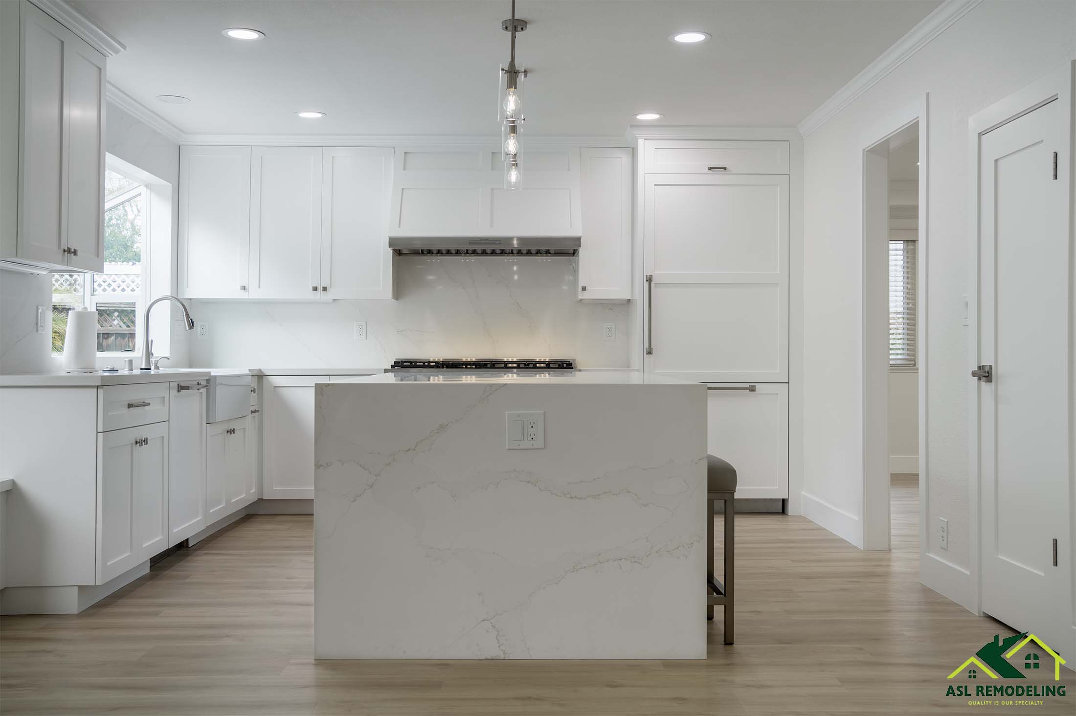 Spacious white kitchen with large quartz island, shaker cabinets, stainless steel appliances, and pendant lighting.