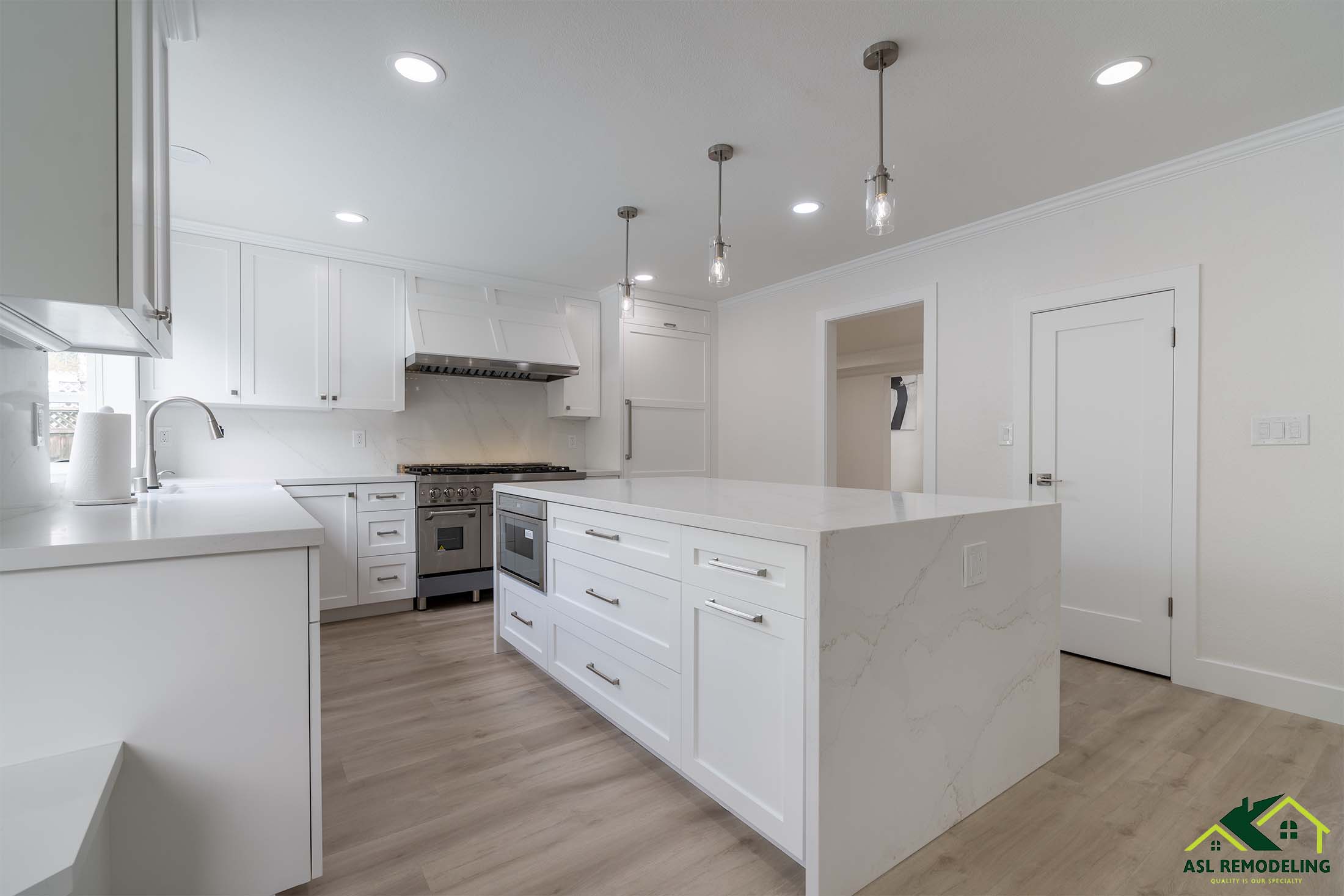 Spacious white kitchen with large quartz island, shaker cabinets, stainless steel appliances, and pendant lighting.