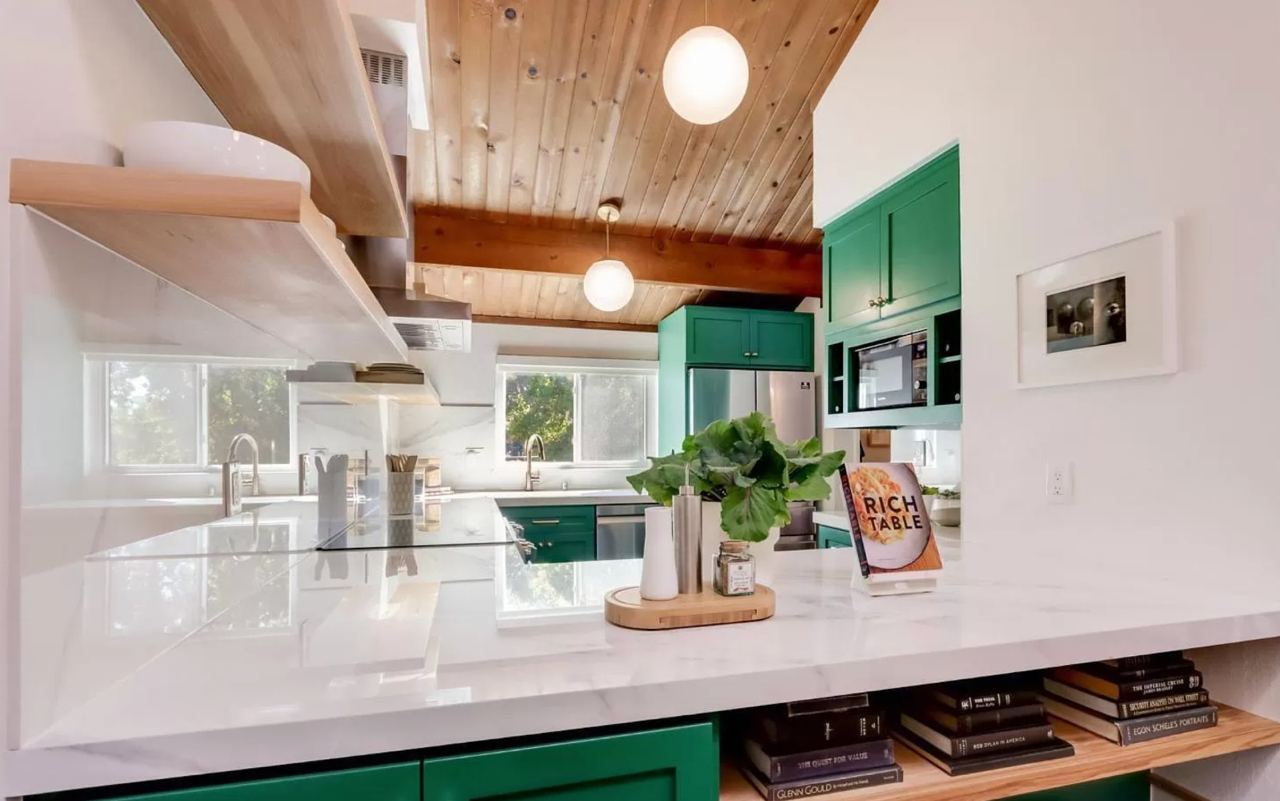 Modern kitchen with green cabinets, wood plank ceiling, white countertops, and open shelving.