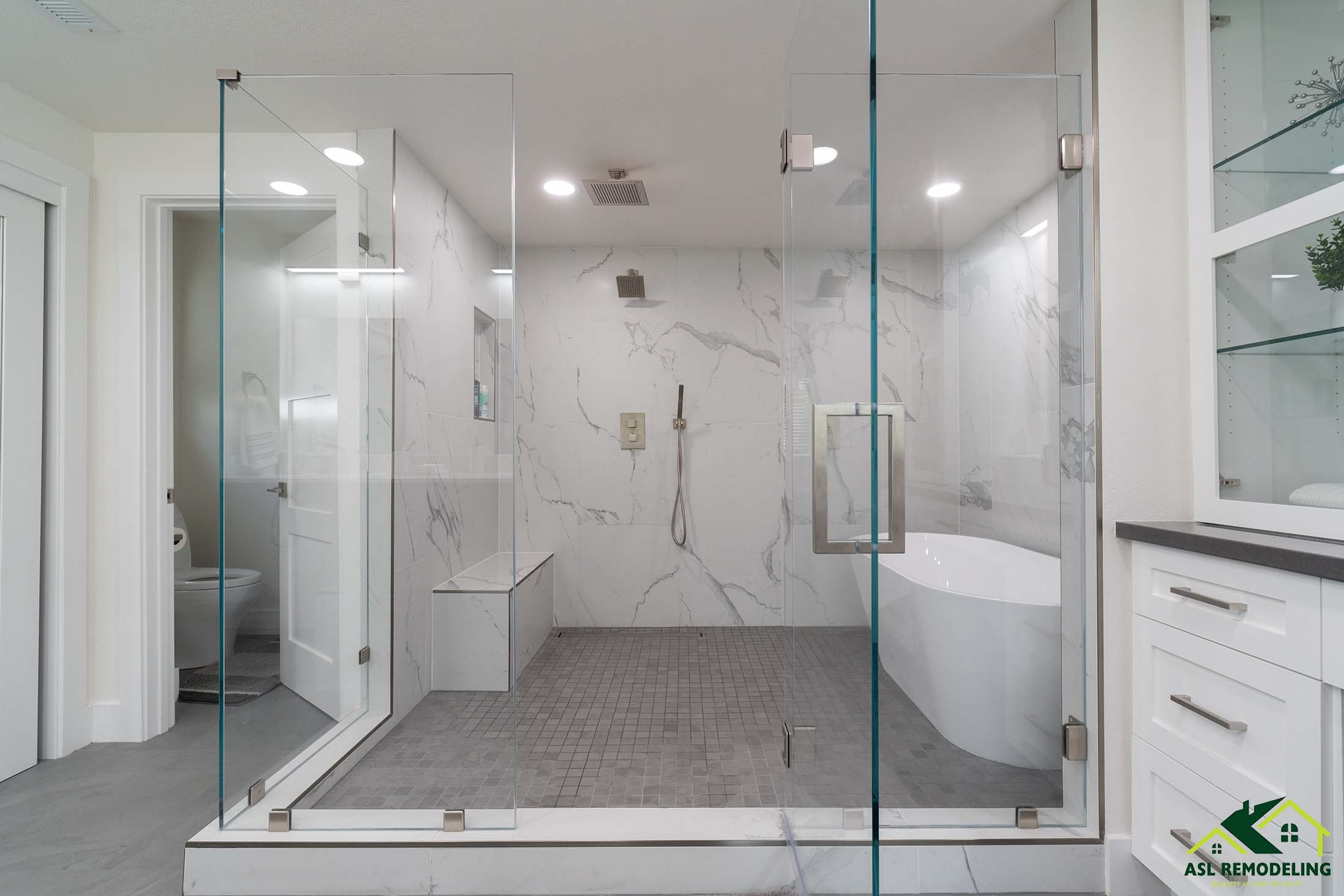 Spacious modern bathroom with large walk-in glass shower, freestanding tub, double vanity with makeup station, and marble accent walls.