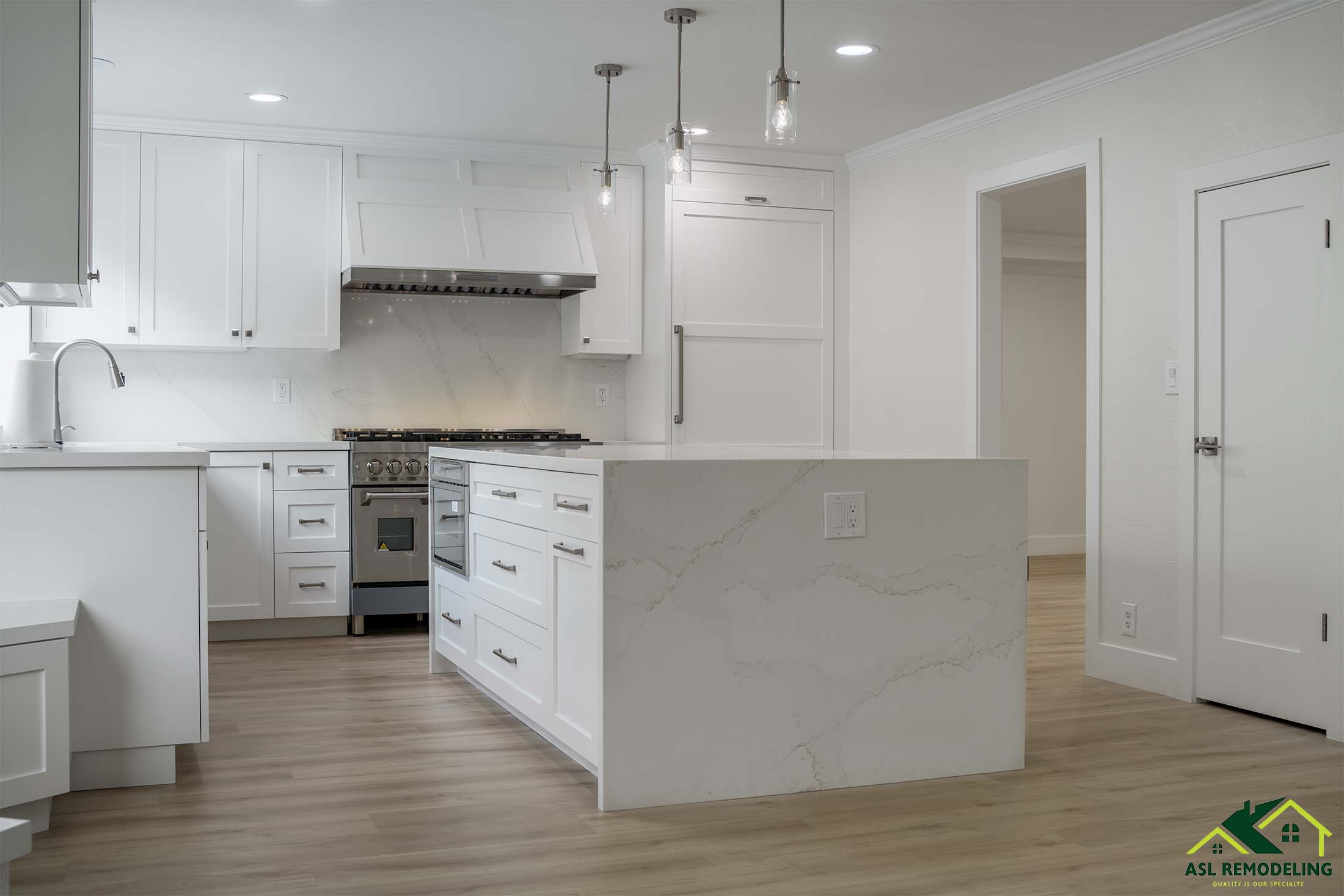 Spacious white kitchen with large quartz island, shaker cabinets, stainless steel appliances, and pendant lighting.