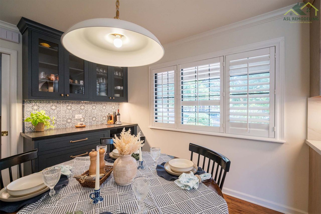 Elegant dining area with a modern touch, featuring a beautifully set table, dark cabinetry with glass panels, patterned backsplash, and natural lighting through plantation shutters. Perfect inspiration for a cozy yet stylish dining space remodel by ASL Remodeling