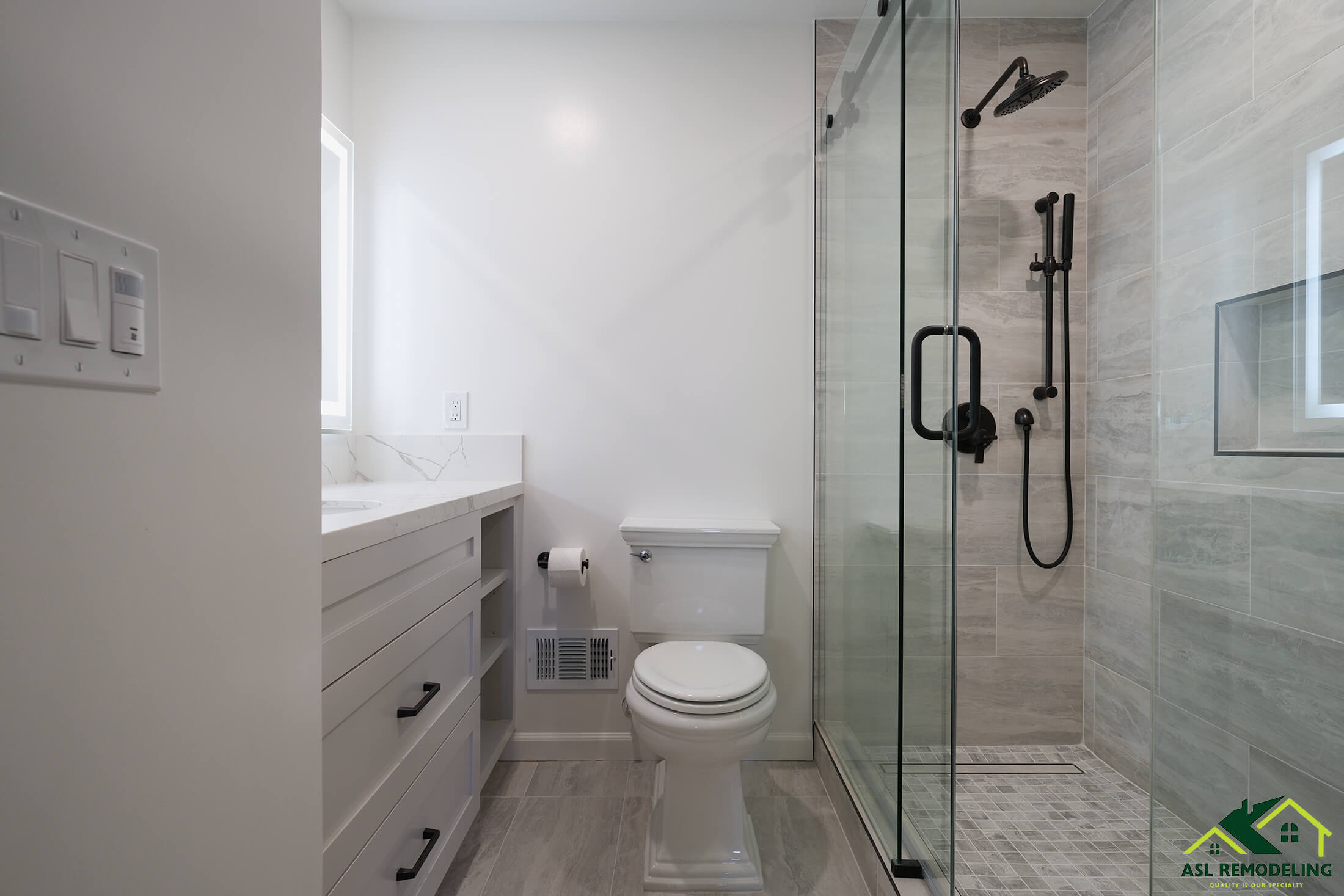 Modern bathroom with white vanity, frameless glass shower enclosure, matte black shower fixtures, and gray tile flooring.