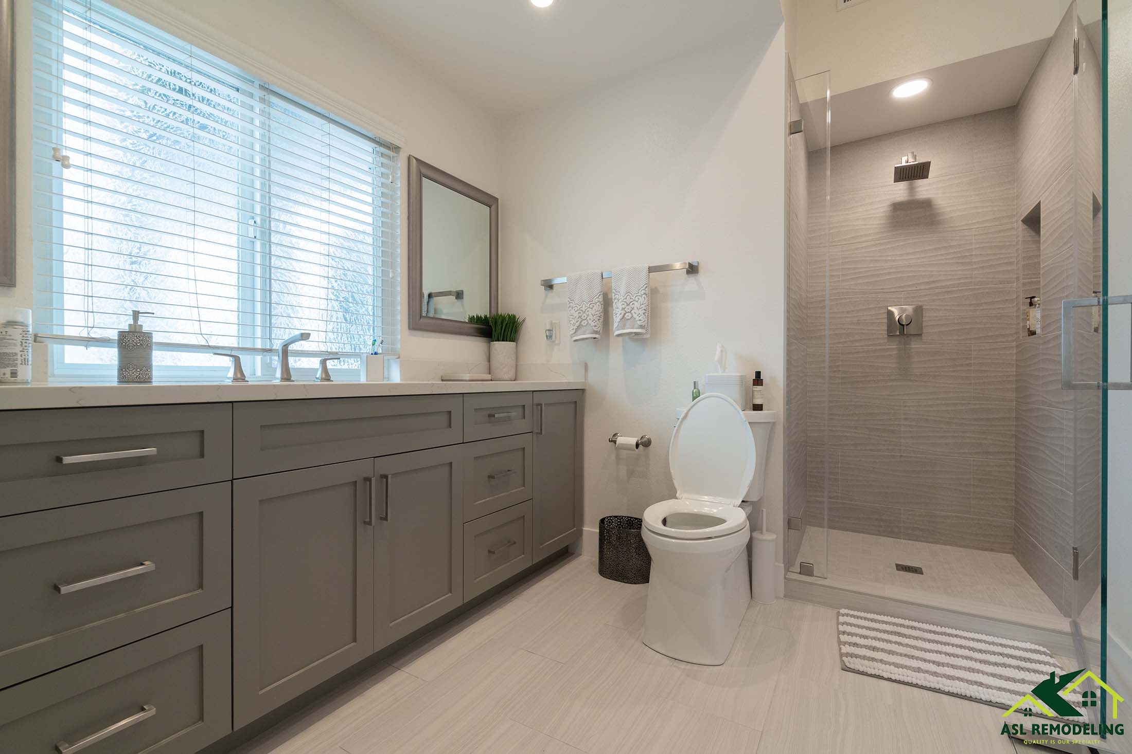 Modern bathroom remodel with walk-in glass shower, light gray shaker vanity, quartz countertop, and natural lighting. Renovated by ASL Remodeling in the Bay Area.