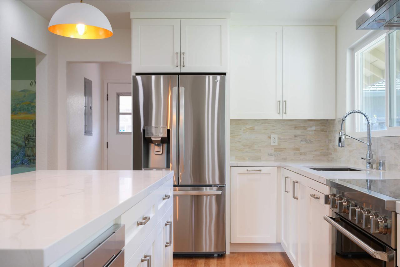 Custom kitchen cabinets in white with dark granite countertops, stainless steel appliances, and statement gold pendant lighting.
