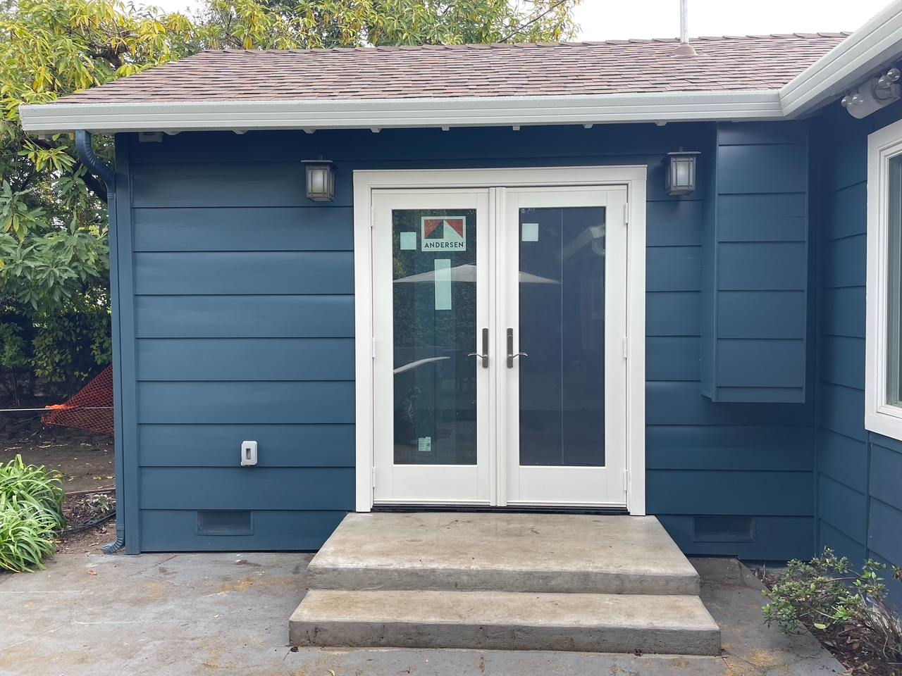 Newly built ADU with blue siding, white double French doors, concrete steps, and exterior wall sconces.